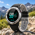A rugged field navigation watch, identical to the one in image_4.png, is set against a blurred background of a rocky mountain trail under a clear blue sky. Natural sunlight creates defined highlights on the metal casing and texturized strap, emphasizing its functional durability and outdoor context. The focus remains sharp on the watch face.